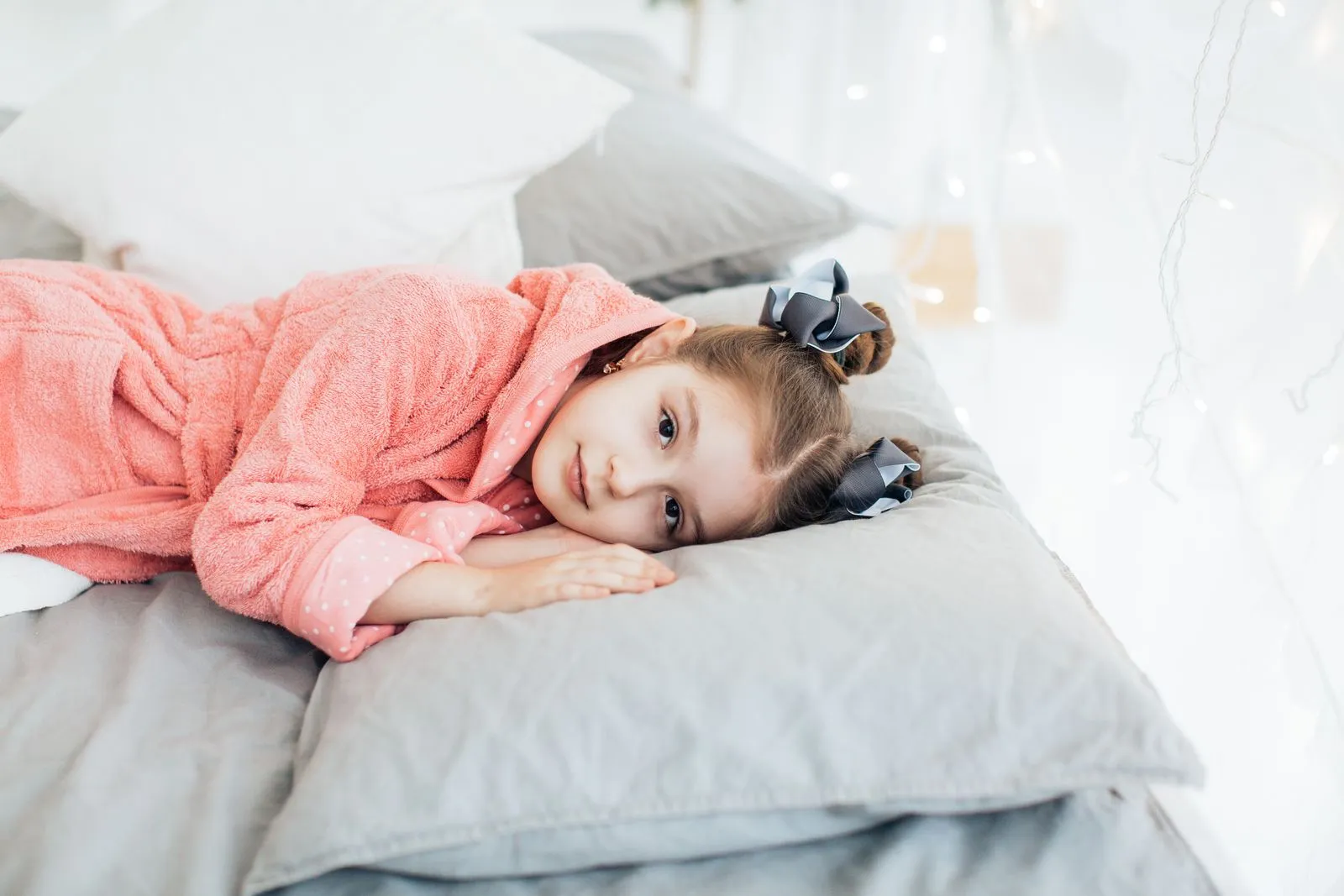 A young girl in a cozy pink robe lying comfortably on a bed with soft pillows.